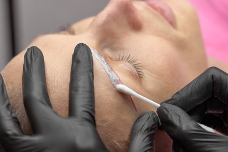 Permanent make up eyeliner procedure, applying on young girl. Close-up. Young beautiful woman making permanent makeup in cosmetology salon. Young girl applying permanent eyeliner in beauty studio.の写真素材