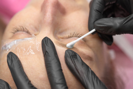Permanent make up eyeliner procedure, applying on young girl. Close-up. Young beautiful woman making permanent makeup in cosmetology salon.の写真素材
