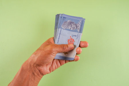 Hand holding Ringgit banknote on a green background.