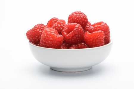 Raspberries in a white ceramic bol on white background