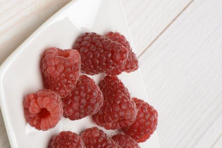 Raspberries on a plate on a white wooden table