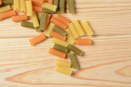 Macaroni in three different colors, raw pasta in wood background