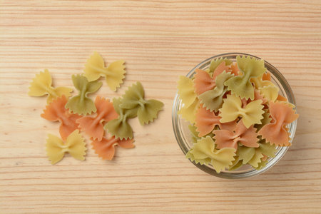 Farfalle pasta in a glass bowl on wooden background