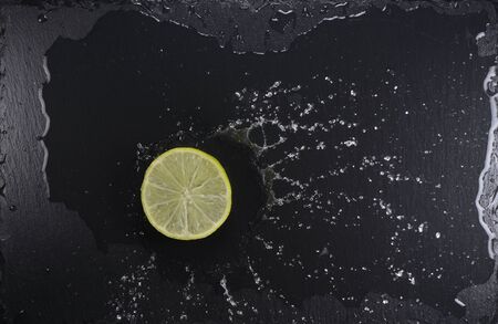 Lemon slice on black stone plate with water splash, top viewの写真素材