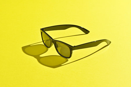 Black sunglasses on yellow background, shadow and lightの写真素材