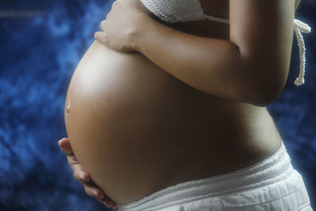 Side view midsection of a pregnant woman with hands holding tummy against blue backgroundの写真素材