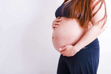 Pregnant lady holding her tummy in black dress and white backgroundの写真素材