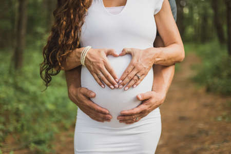 A pregnant lady and her husband hand forming a love shape on the tummyの写真素材