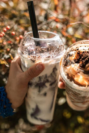 hands holding two milkshakes in transparent plastic cups with tubes in bokeh backgroundの写真素材