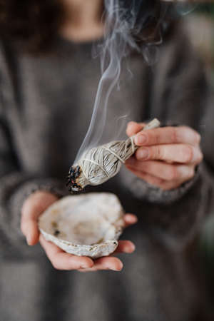 Clearing Energy In Home Using Sage - Smudge Stick - Healing,speckled stick burning in soft focus with bokeh, blurring aroma close-up. Girl's hands hold dried leavesの写真素材