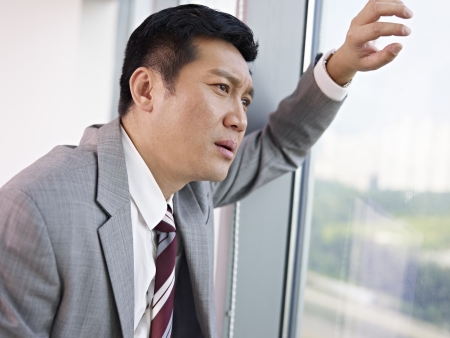 frustrated asian businessman looking out of window in office の写真素材