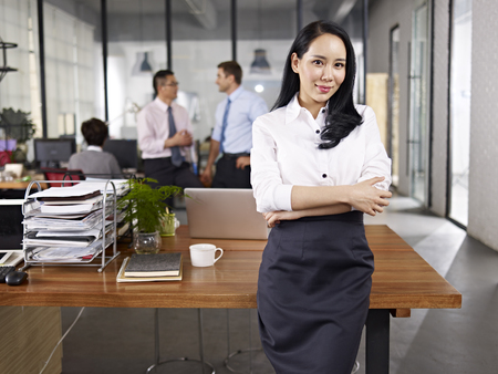 young asian businesswoman standing in office with multiethnic colleagues talking in background.の写真素材