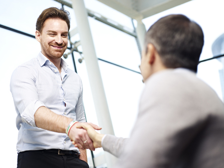 two caucasian businesspersons greeting each other by shaking hands in modern office.の写真素材