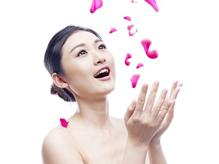 young and beautiful asian woman trying to catch falling petals, isolated on white background.の写真素材