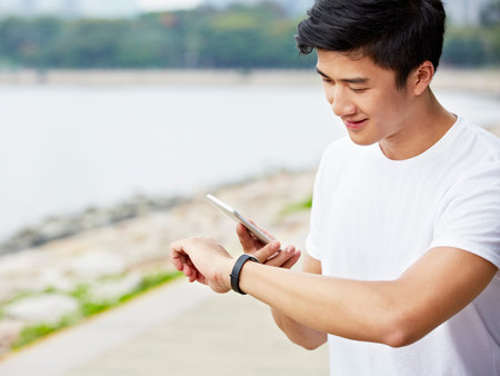 young asian man using apps in smartphone and smartwatch to track fitness data during exercise