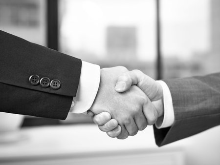 two corporate businessmen shaking hands in office, black and white.