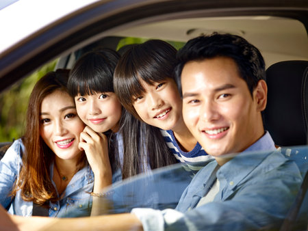 happy asian family with two children riding in a car