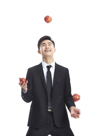 young asian business man wearing suit and tie juggling three apples, isolated on white background.の写真素材