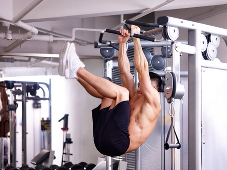 asian bodybuilder exercising abdominal muscle by hanging himself on equipment.