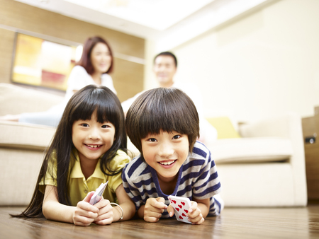 asian brother and sister lying on front on floor with parents in the background.の写真素材