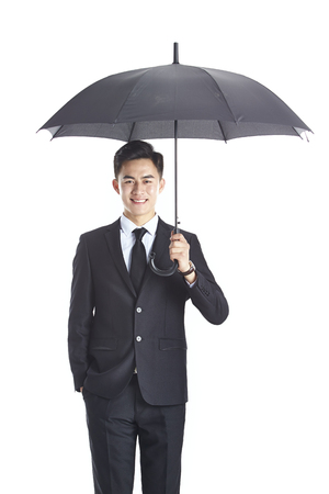 studio shot of a young asian business man holding a black umbrella, happy and smiling, isolated on white background.の写真素材