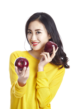 studio shot of a young and beautiful asian woman holding two red apples, isolated on white background.の写真素材