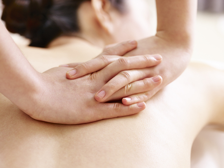 close-up of hands of a masseur massaging back of a young asian womanの写真素材
