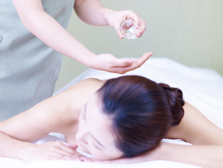 masseuse pouring essential oil on hand while young asian woman lying on front on massage bed.の写真素材