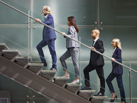 multinational and multiethnic corporate business people male and female walking up stairs in a line in modern office building.の写真素材