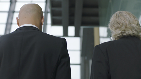 rear view of corporate executives talking while ascending stairs in modern office buildingの写真素材