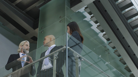 three multinational company executives standing on second floor of modern office building discussing business.の写真素材