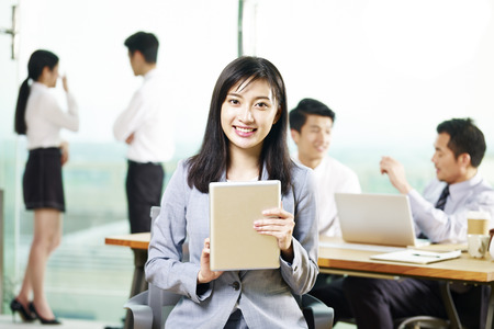 portrait of young asian business woman holding digital tablet looking at camera smiling in office.の写真素材