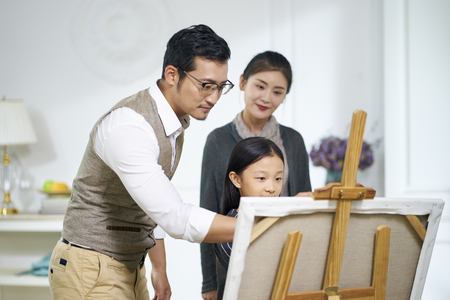 little asian girl making a painting getting help from father while mother watching in the backgroundの写真素材