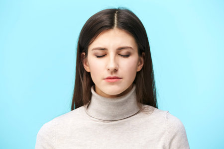 portrait of a young caucasian woman, eyes closed, isolated on blue background