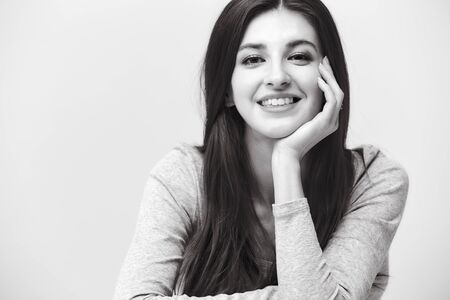 black and white portrait of a beautiful caucasian woman, hand on cheek, looking at camera smilingの写真素材
