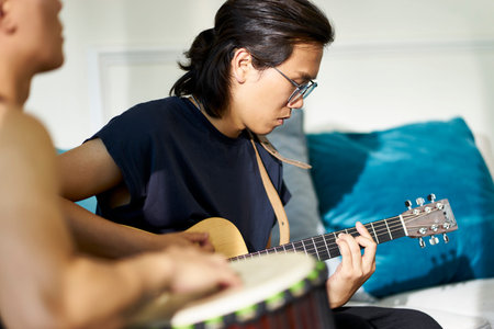 young asian  guitarist sitting on couch playing guitar