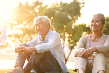asian senior couple sitting on grass enjoying sunset outdoors in park