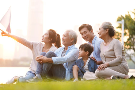 three generation happy asian family sitting on grass enjoying good time at dusk outdoors in parkの写真素材