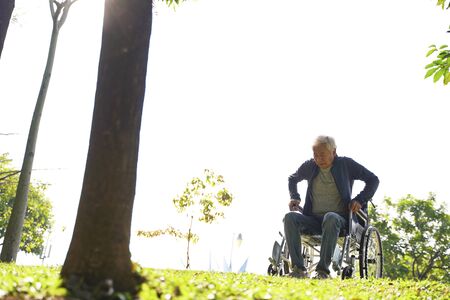 senior asian man trying to  get up from wheelchair outdoorsの写真素材
