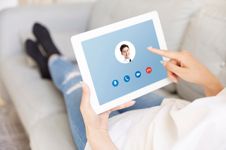 young asian woman working at home answering a video call from colleague using digital tablet
