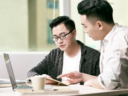 two young asian entrepreneurs discussing business in office using digital tablet and laptop computer