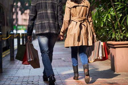 rear view of young asian couple walking on street with shopping bags in handsの写真素材