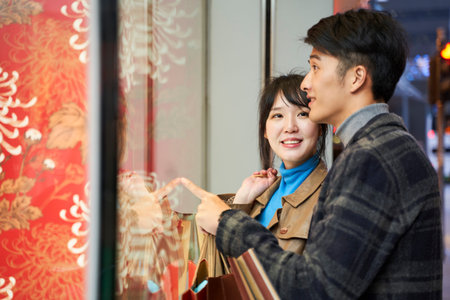happy young asian couple looking into shop window in modern city
