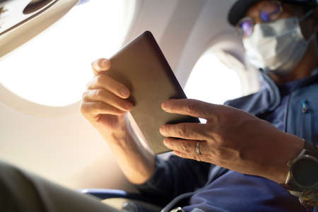 asian man male passenger sitting in cabin of airplane reading ebook using e-readerの写真素材