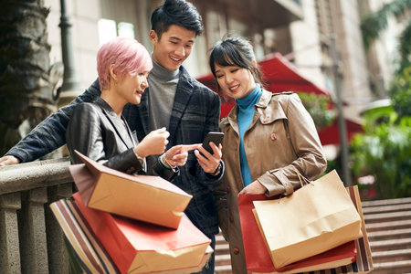 three young asian fashionable people navigating using cellphone while shopping in the city