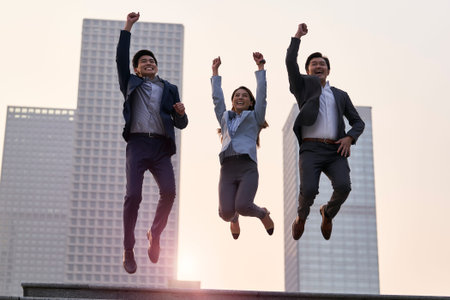 team of three asian corporate executives jumping celebrating success and achievement with city backgroundの写真素材