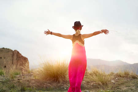 rear view of a young asian woman in red dress embracing the morning sunlight in a deserted mountain areaの写真素材