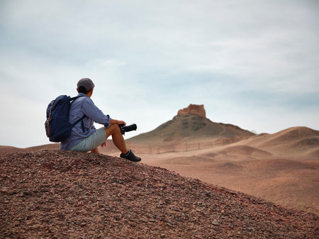 asian male backpacker landscape photographer sitting on top of a hill looking at view, side view