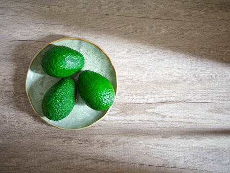 three green avocados on plate on wooden surface