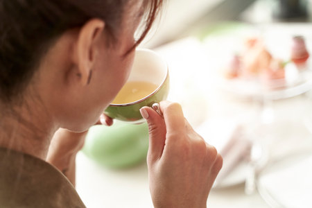 close-up rear side view of an asian woman sitting at table drinking tea from a green teacupの写真素材